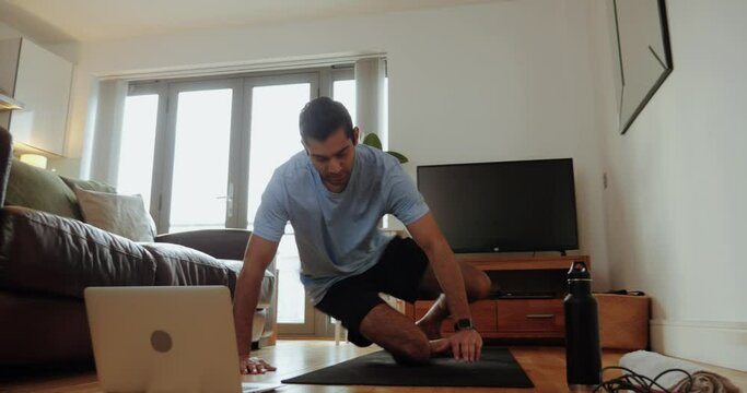 Mixed race male sitting on floor in living room preparing for exercise holding plank