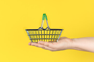A basket for groceries and purchases in green from a hypermarket, miniature in hand on a yellow...