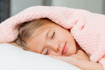 little blonde girl sleeping in bed under a pink knitted blanket, space for text