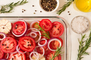 Top view of sliced tomatoes, garlic, onion, and rosemary in a glass oven dish. Mediterranean food
