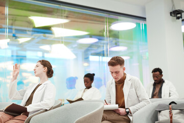 Fototapeta premium Side view at group of young people wearing lab coats while sitting in audience and listening to lecture on medicine in college or coworking center, copy space