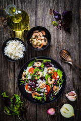 Prawn salad with white rice, lettuce, cherry tomatoes and onion on wooden background
