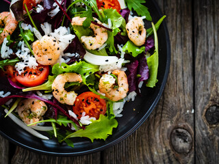 Prawn salad with white rice, lettuce, cherry tomatoes and onion on wooden background