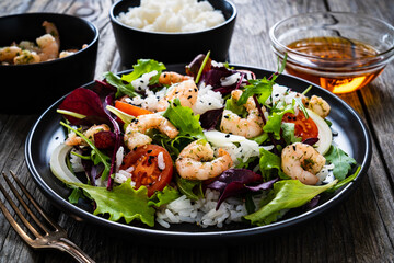 Prawn salad with white rice, lettuce, cherry tomatoes and onion on wooden background
