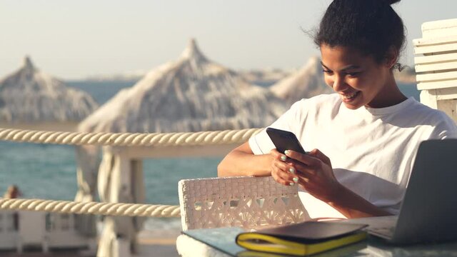 Cheese. Cool young woman taking selfie and sending it to her friends and colleagues using smartphone while relaxing on the beach resort, working remotely. Freelance work, travel concept
