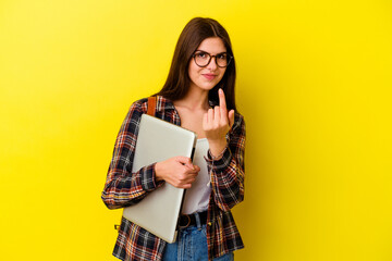 Young caucasian student woman holding a laptop isolated on pink background pointing with finger at you as if inviting come closer.