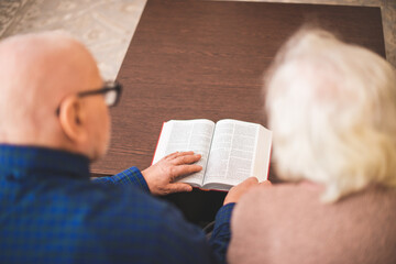 Elderly couple reading bible and pray together at home.