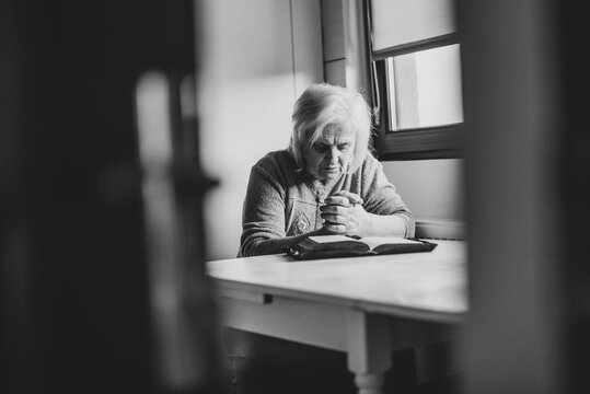 Old woman spending time alone with god, praying and reading bible.