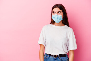 Young caucasian woman wearing a mask for virus isolated on pink background being shocked because of...