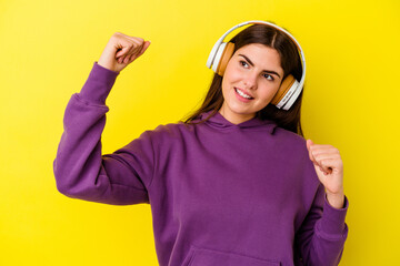 Young caucasian woman listening to music with headphones isolated on pink background raising fist after a victory, winner concept.