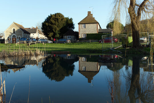 East Dean village pond with reflections in the water of trees and cottages in this traditional English Village situated in the beautiful countryside of West Sussex.