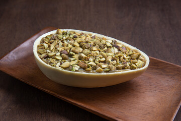 Stuffed pistachio and white chocolate easter egg on a wooden stand on a wooden table.