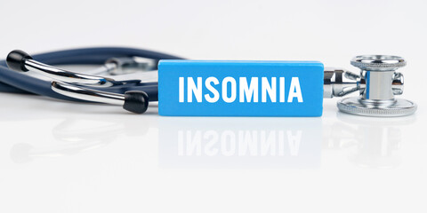 On a white reflective surface is a stethoscope and a blue Jenga with the inscription - INSOMNIA