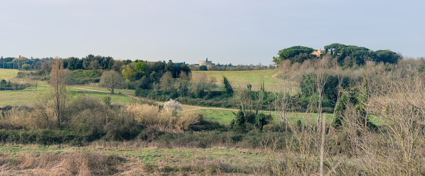 Panorama of typical Italian countryside landscape in Caffarella Appian Way public park, an archeological site with ancient Roman ruins like the tomb of Caecilia Metella and a church, in Rome, Italy