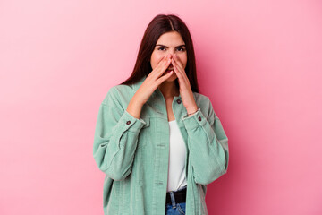 Young caucasian woman isolated on pink background saying a gossip, pointing to side reporting something.