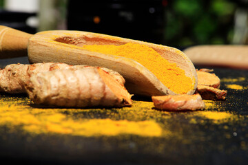Turmeric powder in a wooden spoon and roots on a dark table (curcuma longa), Kurkuma