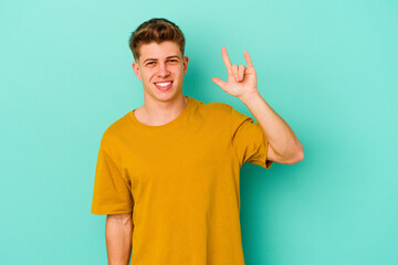 Fototapeta premium Young caucasian man isolated on blue background showing a horns gesture as a revolution concept.