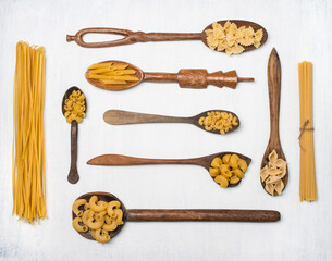 Different types of pasta in vintage  old wooden spoons on white background. Variety of dry pasta set. Flat lay.