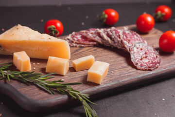 Smoked ham sausage and cutted slices with rosemary, cherry tomatoes and cheese parmesan on dark wooden board