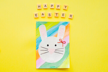 HAPPY EASTER text wooden letters and Hand-made Easter card on yellow background. Top view. Easter concept. 