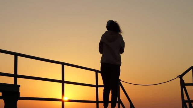 Freedom and happiness. Young woman standing on the sea pier with raised up arms at sunrise. Nature, travel, vacation concept