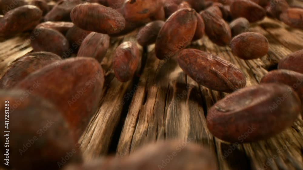 Poster super slow motion of falling group of cocoa beans on wood, camera follow. filmed on high speed cinem