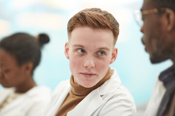 Close up portrait of young man wearing lab coat while sitting in row in audience and listening to lecture on medicine in college, copy space