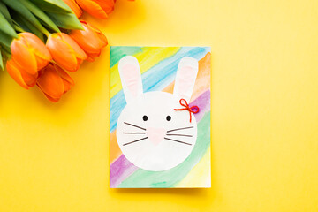 Hand-made Easter card and orange tulips on yellow background. Top view. Easter concept. 