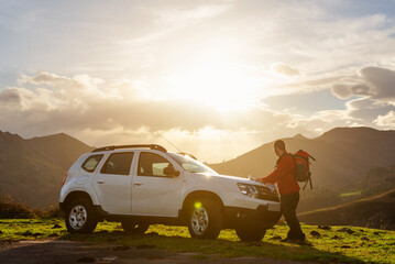 Hiker with backpack looking at a map on the hood of his off-road car at sunset. Traveler and...