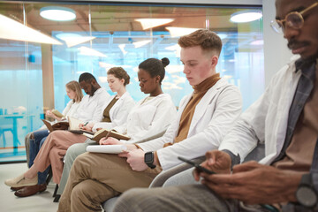 Obraz premium Multi-ethnic group of people wearing lab coats while sitting in row and taking notes during lecture on medicine in college, copy space