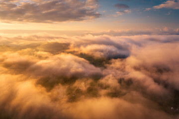 Mountains in clouds at sunrise in summer. Aerial view of mountain peak in fog. Beautiful landscape with high rocks, forest, sky. Top view from drone of mountain valley in low clouds. Foggy hills