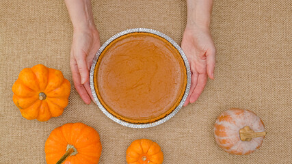 Fresh baked pumpkin pie in disposable baking pan close up in woman hands on rustic background