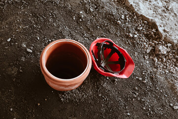 Construction building site background with plastic tube in ground for columnar foundation and red helmet at rushed stones surface