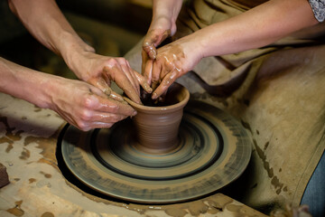 Fototapeta na wymiar Pottery classes, student making clay pot on wheel. Close-up of dirty hands, sculpting clay crockery pottery training