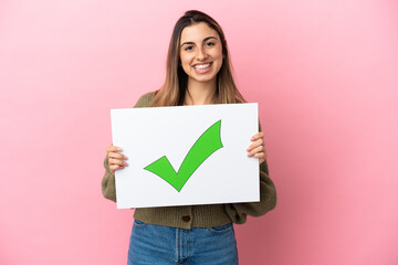 Young caucasian woman isolated on pink background holding a placard with text Green check mark icon...