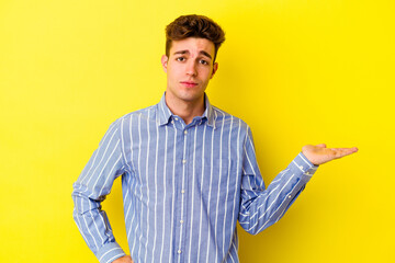 Young caucasian man isolated on yellow background doubting and shrugging shoulders in questioning...