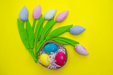Easter card with painted eggs in nest and colorful tulips. Top view and flatly on yellow background