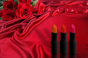 Obraz na płótnie Canvas set of lipsticks on a background of luxury red silk, flower buds, roses, concept of decorative cosmetics