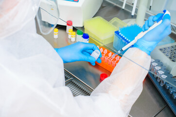 a female PCR laboratory researcher in a protective medical suit, sterile mask, helmet, rubber...