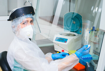 a female PCR laboratory researcher in a protective medical suit, sterile mask, helmet, rubber...
