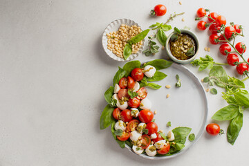 Classic italian caprese salad in grey ceramic plate with fresh tomatoes,mozzarella,basil,pine nuts,pesto and fresh oregano.Foodstyling.Top view with copy space.