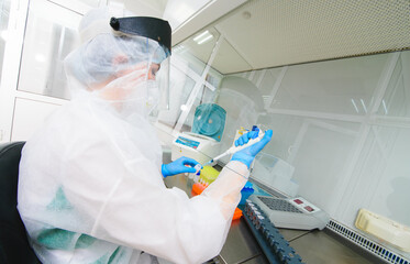 a female PCR laboratory researcher in a protective medical suit, sterile mask, helmet, rubber gloves with a dispenser in her hands conducts a scientific experiment or develops a vaccine.