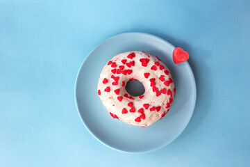 White donut sprinkled with small pink hearts and placed on a beautiful blue plate. Blue background.