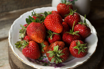 Ripe strawberries in a white old plate, near a rose. Brown wooden background