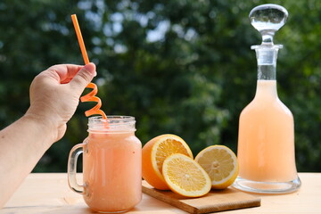 fresh fruit smoothies in a decanter and a mug on a background of green garden foliage, orange...