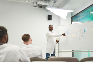 Obraz premium Wide angle view at African-American man standing by whiteboard while giving seminar on medicine in college, copy space