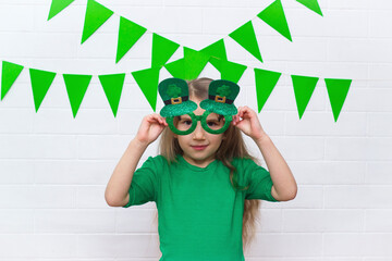 Portrait of a smiling Caucasian girl in a green T-shirt with clover leprechaun glasses on St....