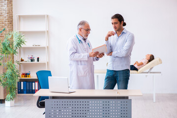 Fototapeta premium Small girl with her father visiting old male doctor