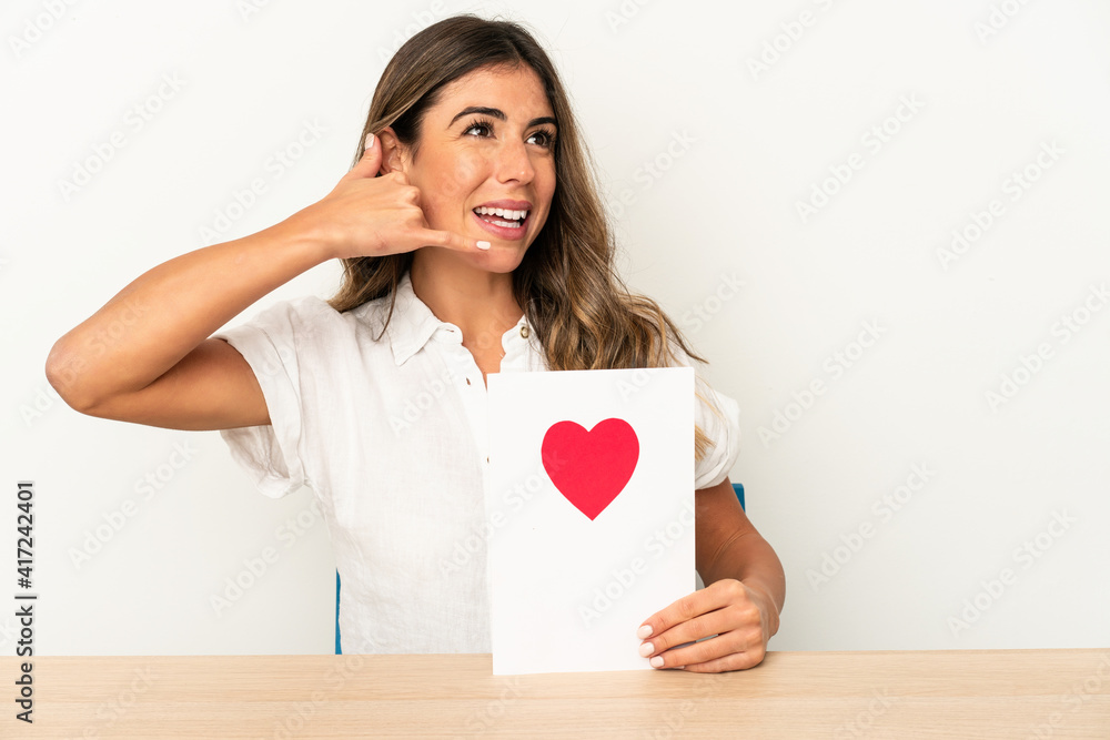 Wall mural young caucasian woman holding a valentines day card isolated showing a mobile phone call gesture wit