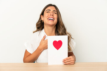 Young caucasian woman holding a valentines day card isolated laughs out loudly keeping hand on chest.